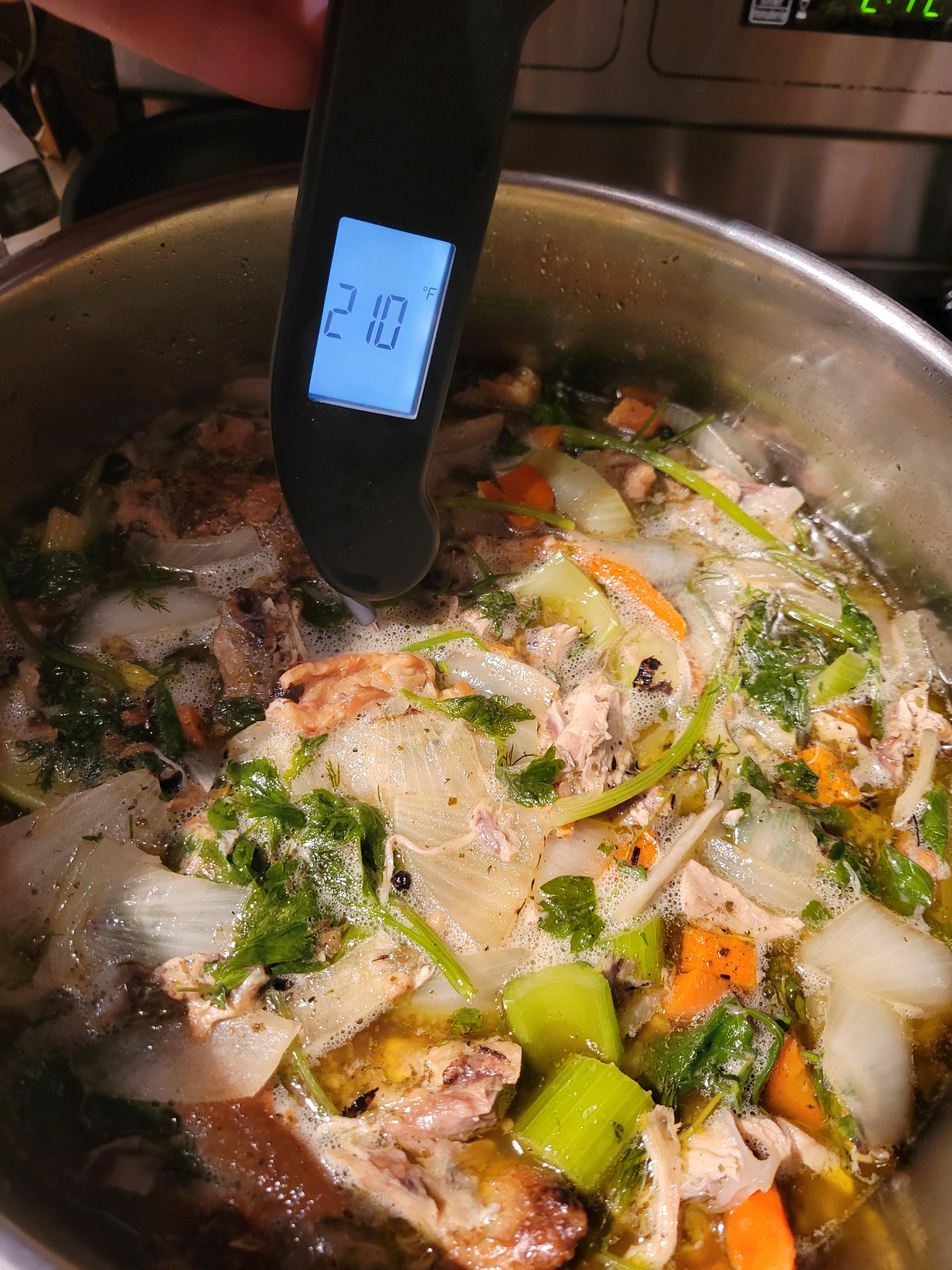 Куриный бульон медленно кипит в кастрюле с костями и овощами