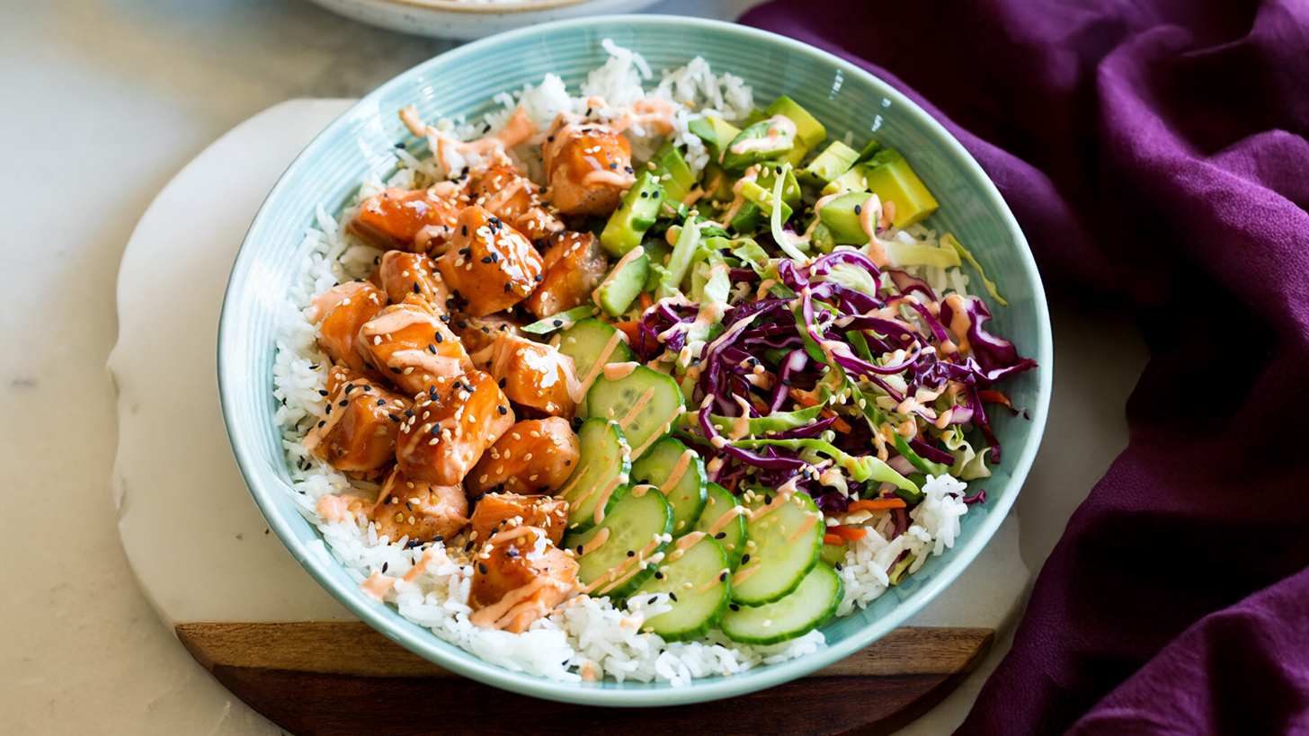 Рис в миске, сверху кубики лосося, авокадо и огурца.